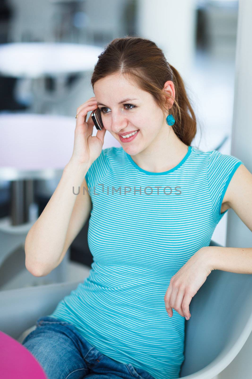 Pretty young woman using her mobile phone/speaking on the phone in a public area (shallow DOF; color toned image)