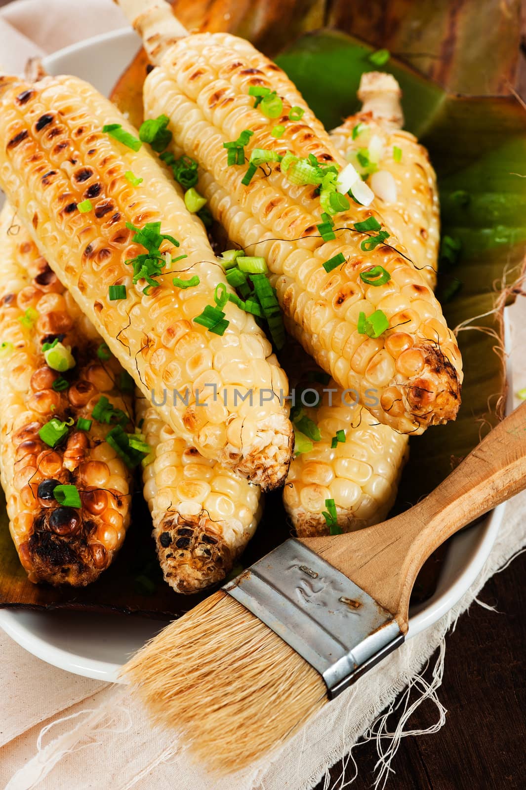 Barbecued corn cobs with herbs on a white plate and a wooden table