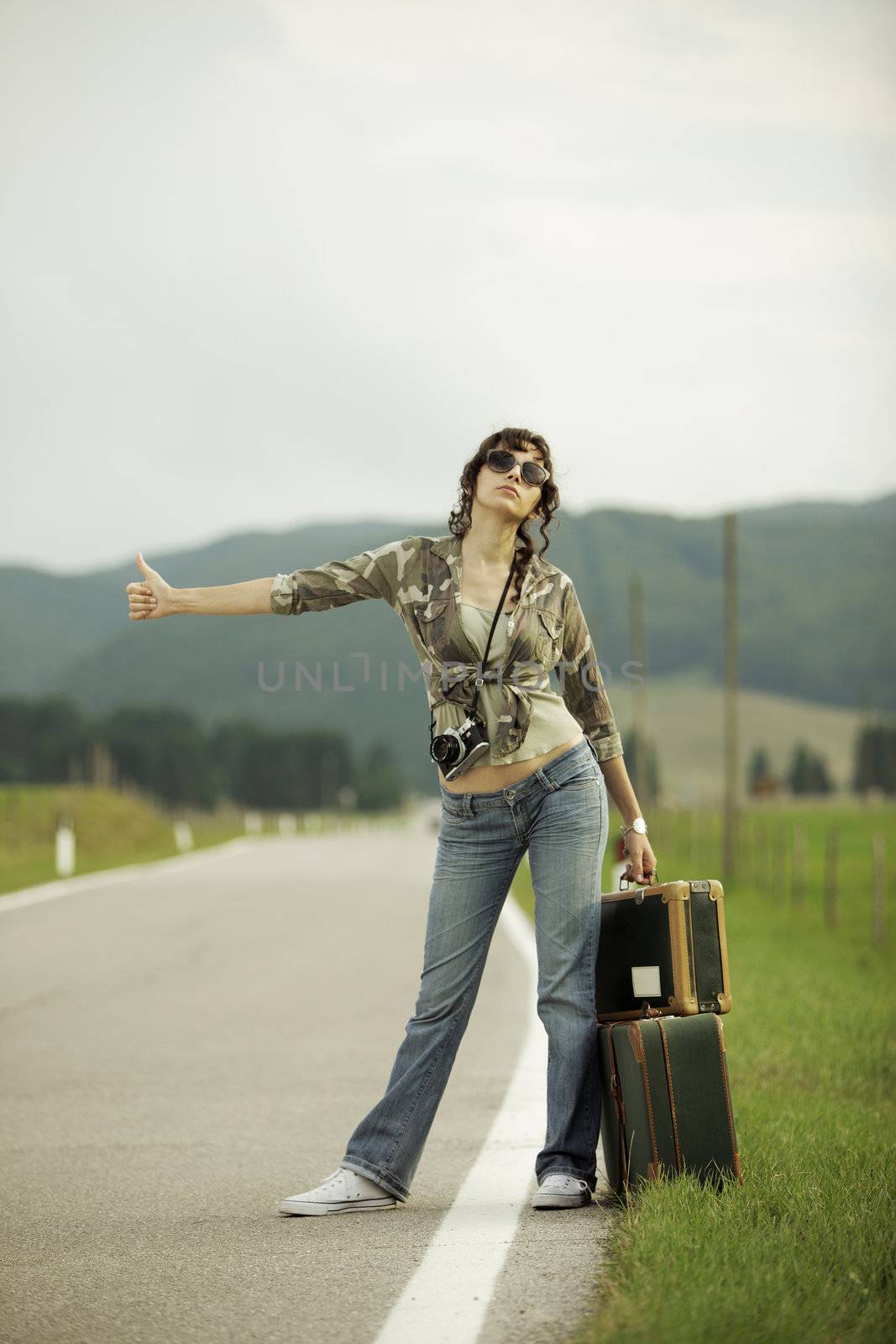 A woman hitchhikes on the side of the road.