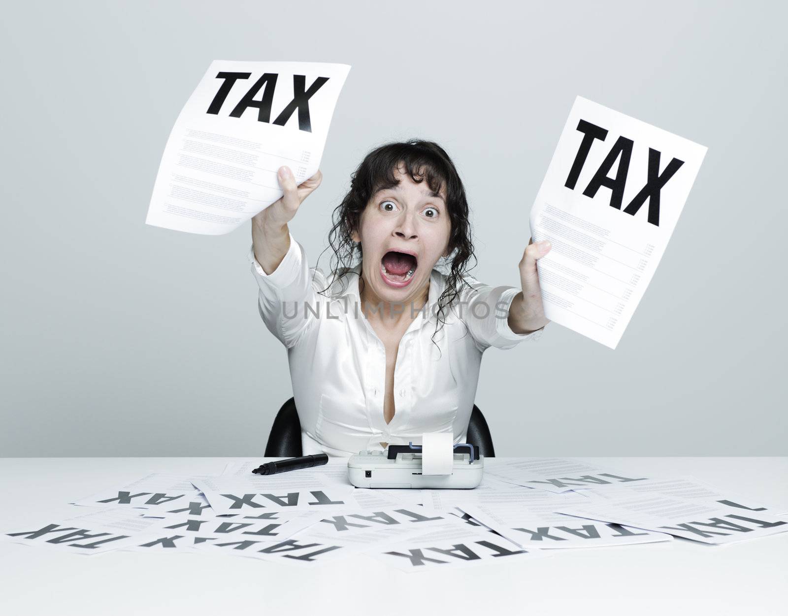 Young desperate woman at her desk showing terrible tax bills to the camera while shouting out