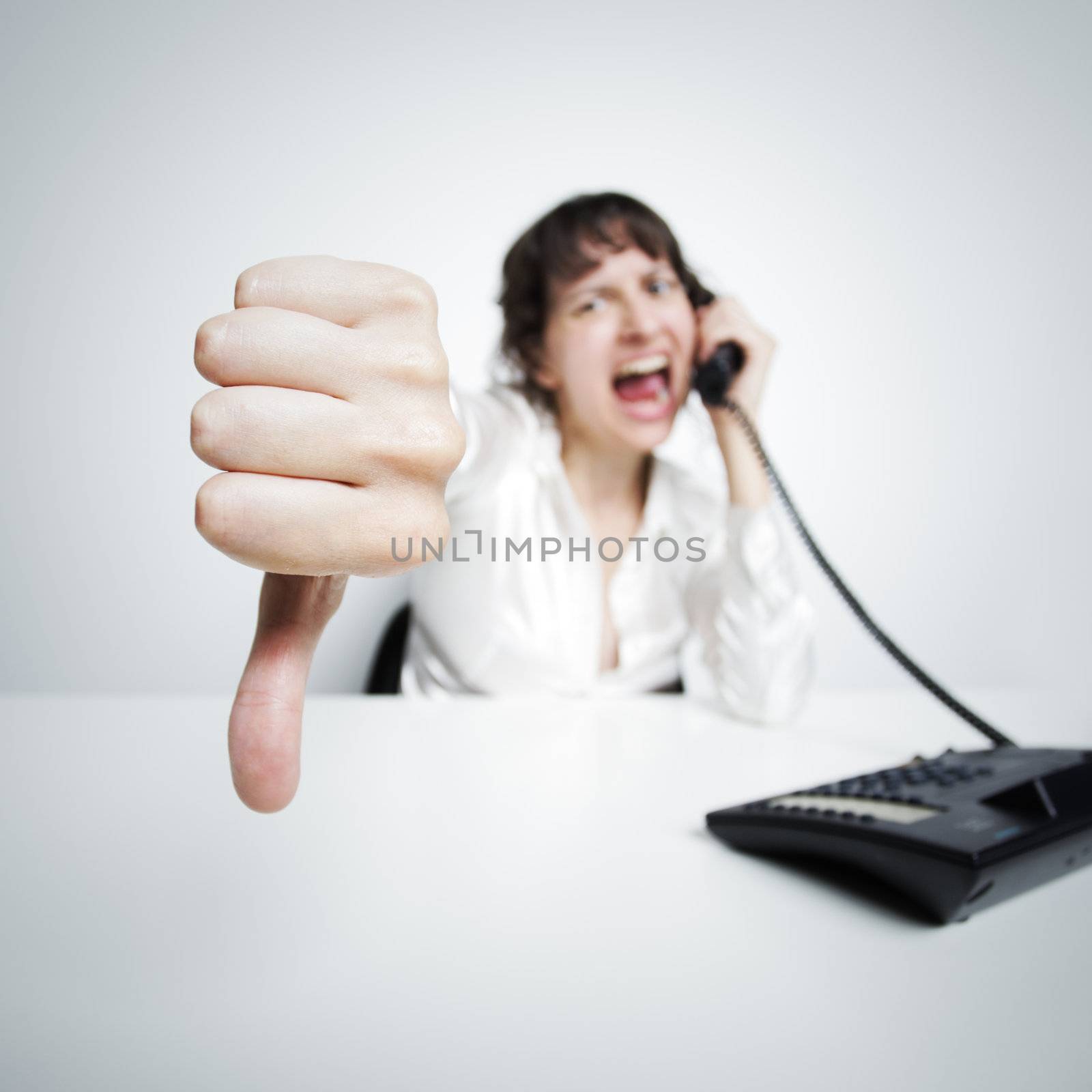 an hostile woman shows thumbs down against us (at the camera) while phoning at her office desk