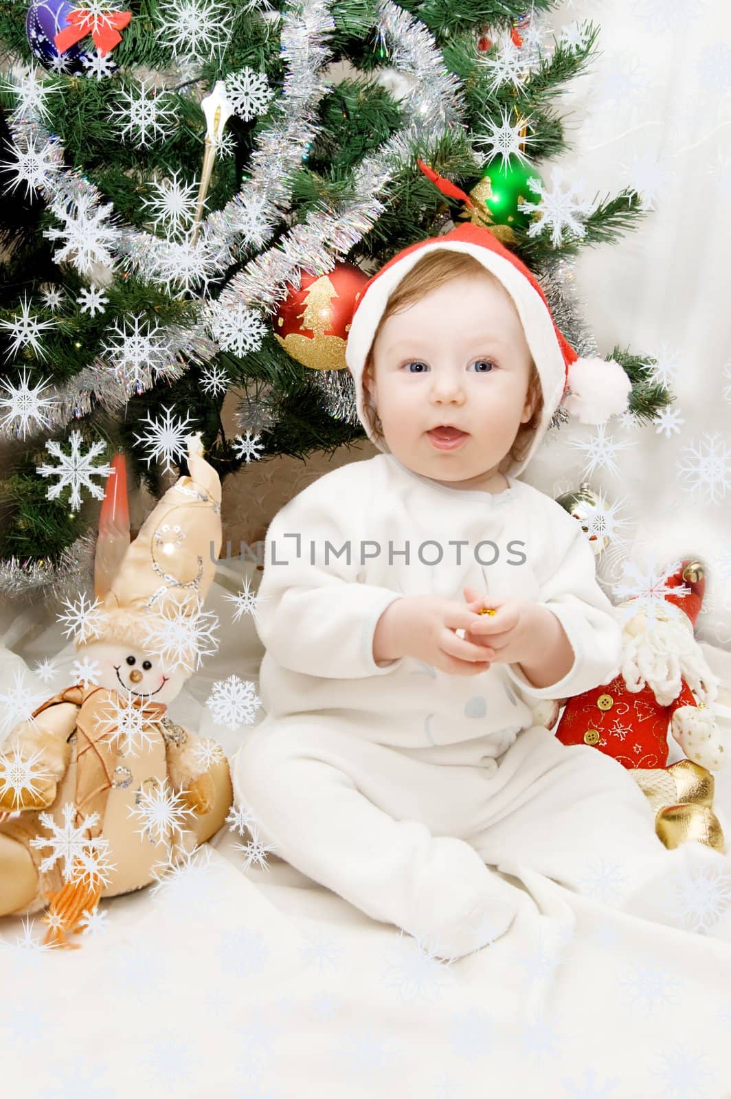 Baby in santa hat sitting under Christmas tree