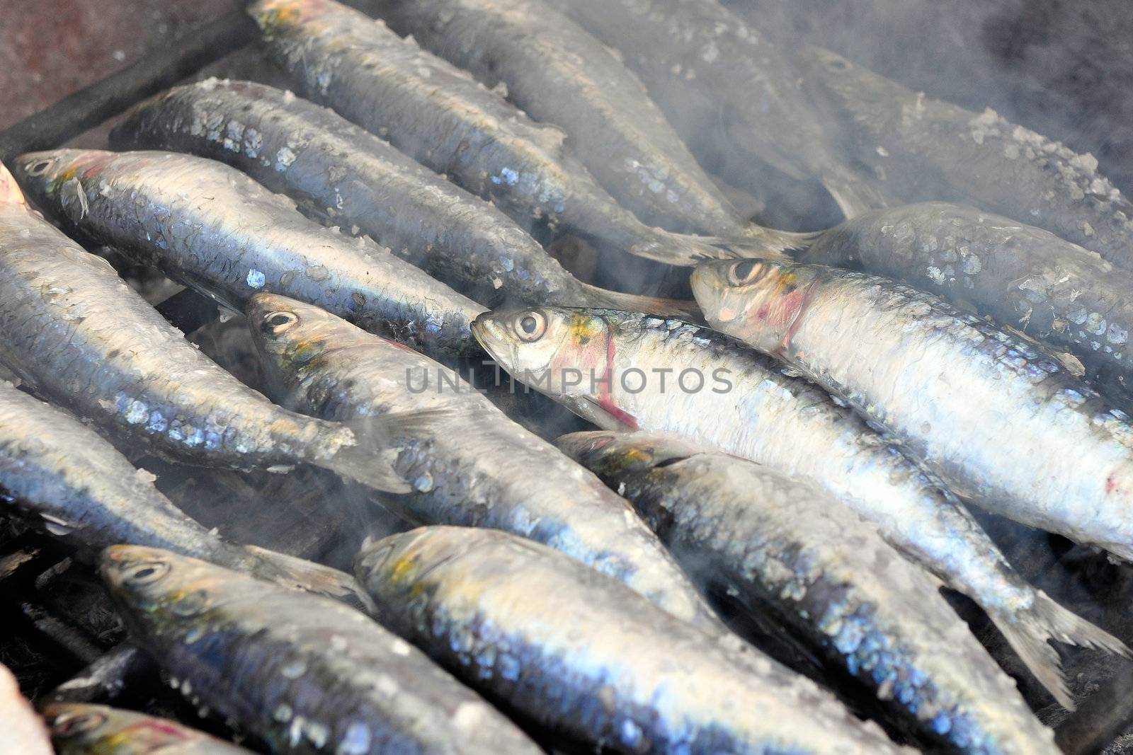 Fresh sardines being grilled in a charcoal grill with smoke around
