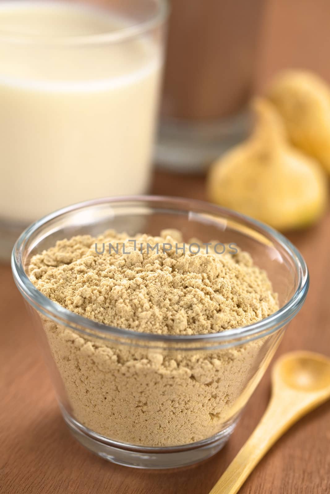 Powdered Maca or Peruvian ginseng (lat. Lepidium meyenii) in glass bowl with milk, chocolate drink and maca roots in the back (Selective Focus, Focus one third into the maca powder)