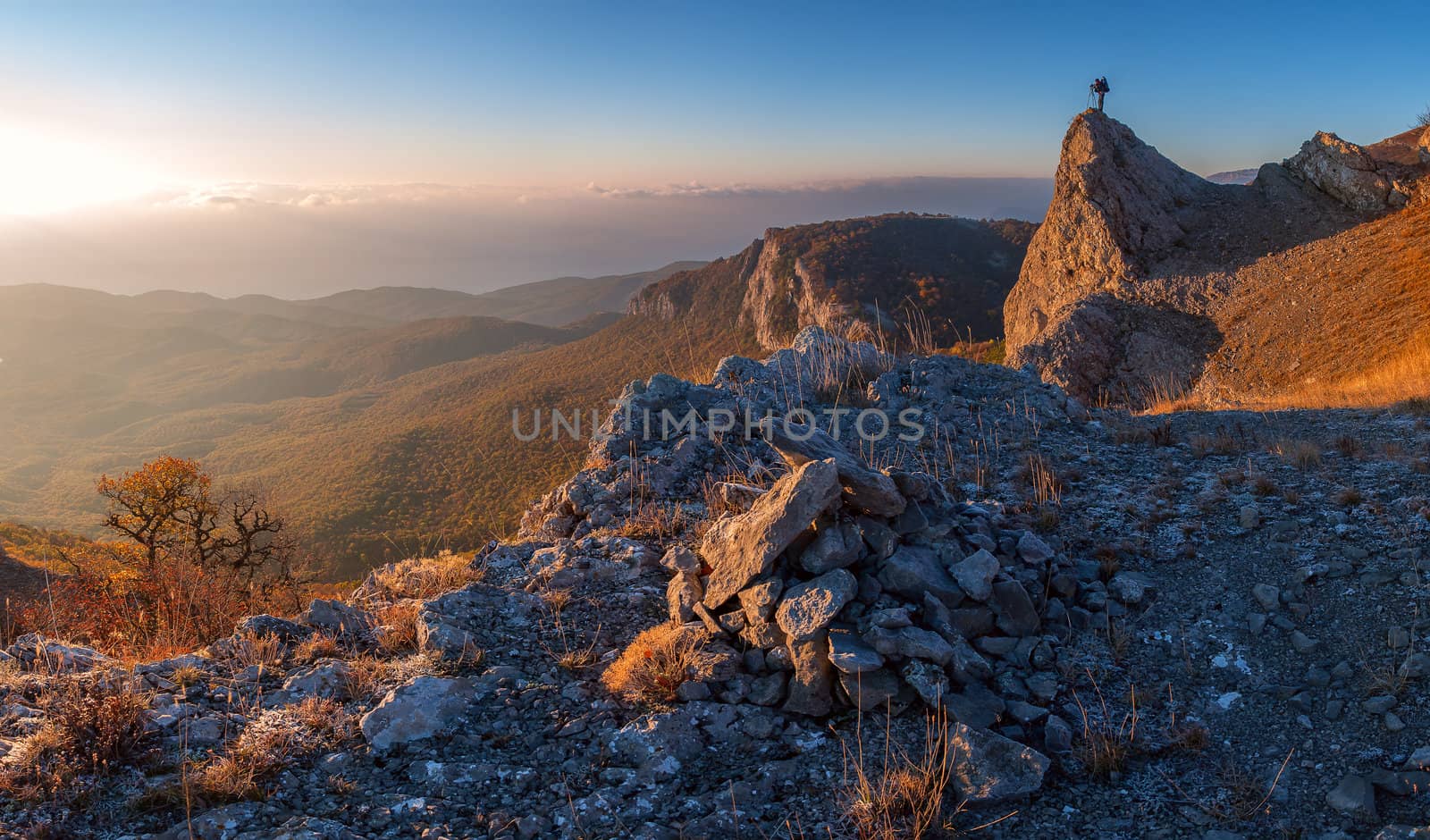 A man standing at mountain top with camera against a beautiful sunrise