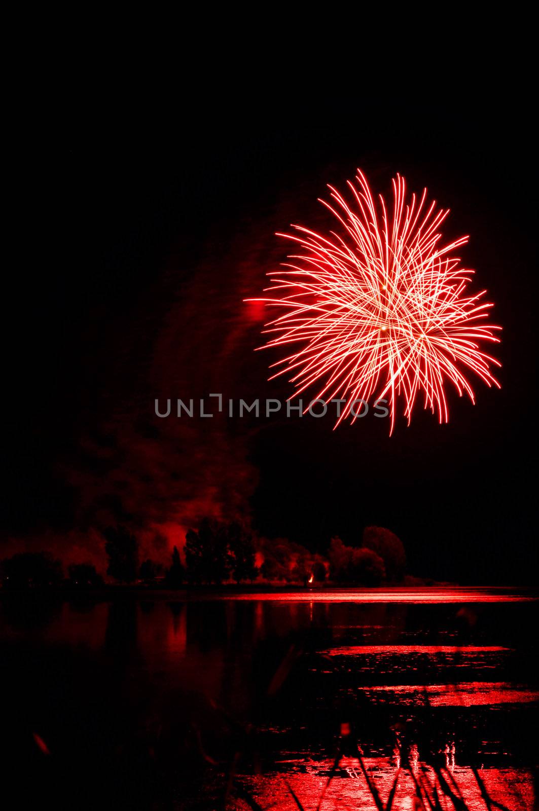 Beautiful red firework over a lake with reflections, perfect black sky as copy space for text.