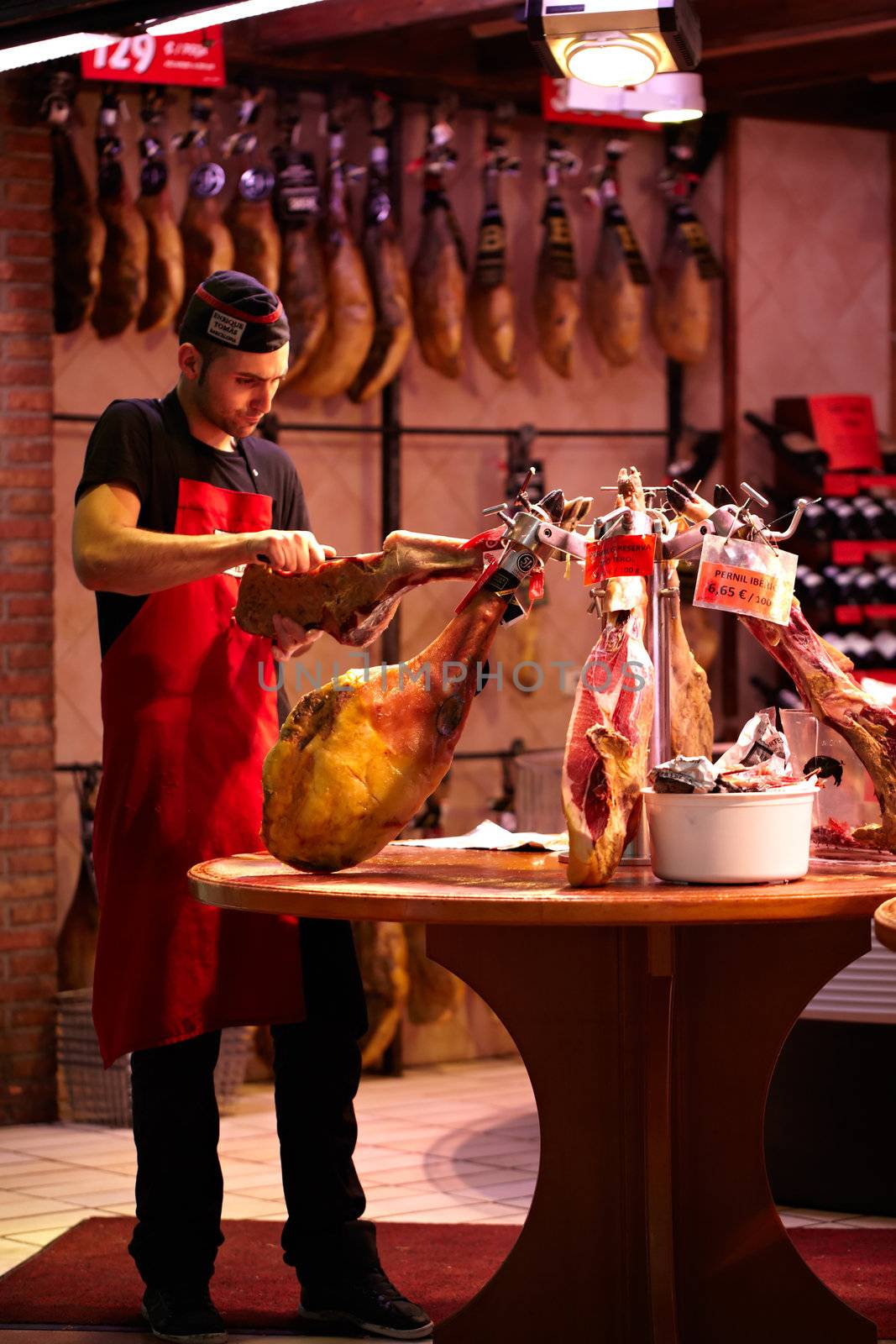BARCELONA - MAY 21: Young man, a jamon seller, in a robe and cap is cutting meat in the supermarket on May 21, 2012 in Barcelona, Spain.