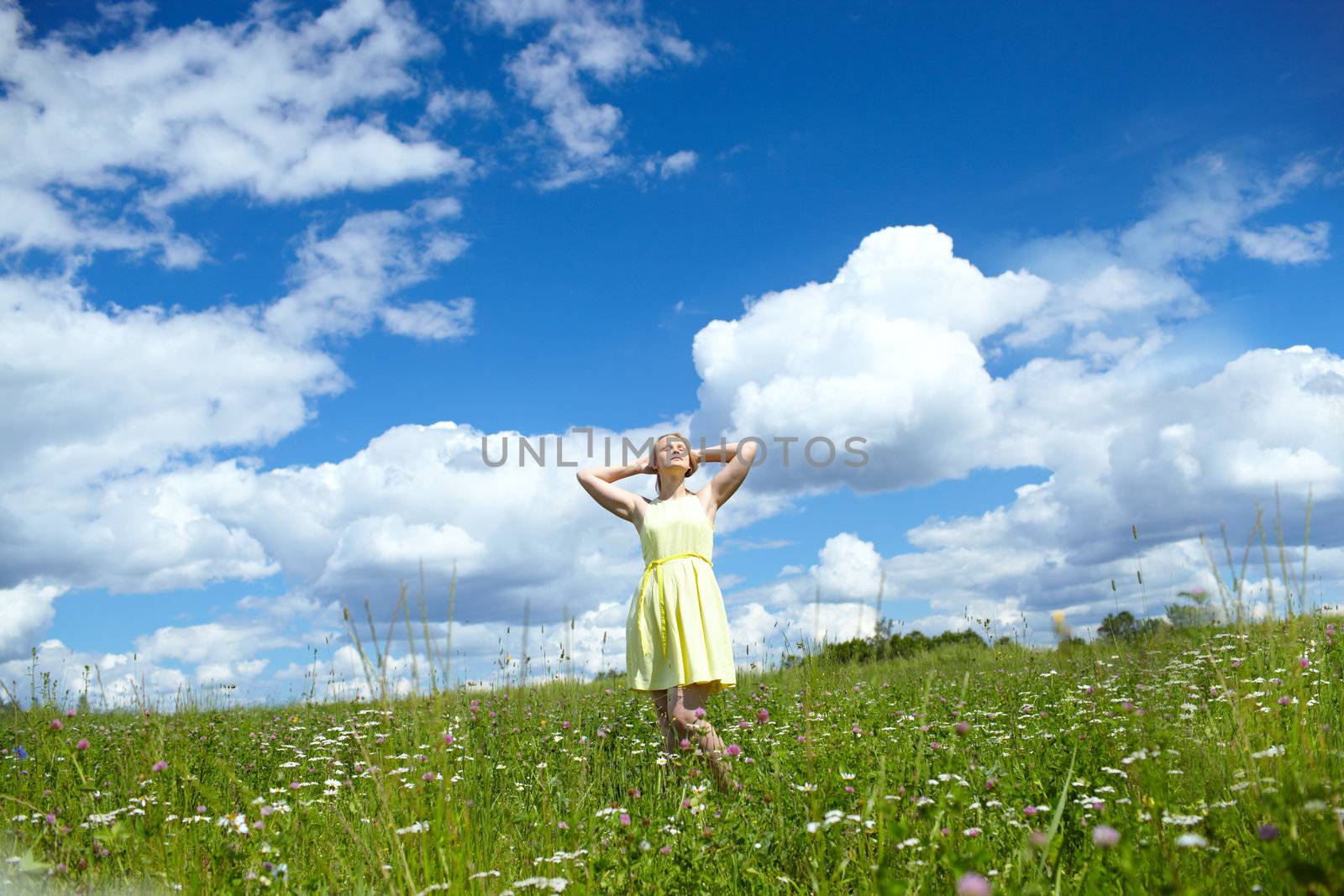 A girl in a yellow dress is lying in the sun in the field with meadow flowers.