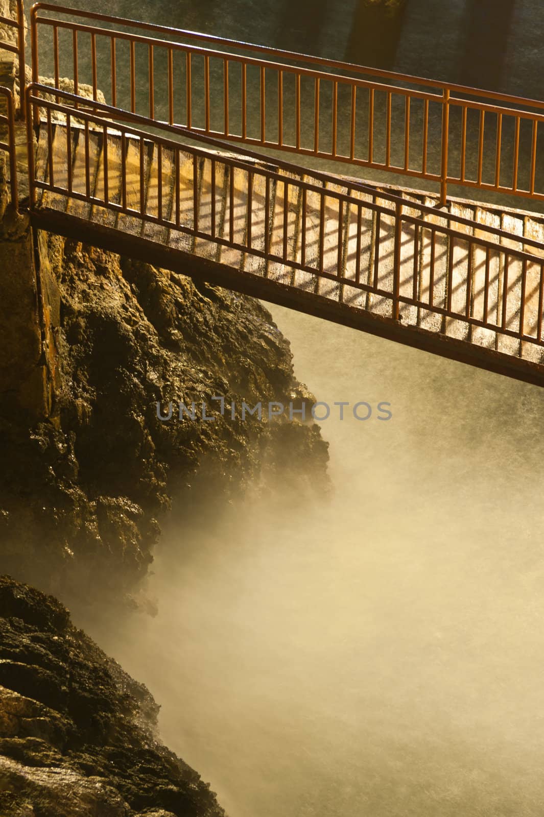 Narrow wooden steel bridge over the wild river and rocks at night