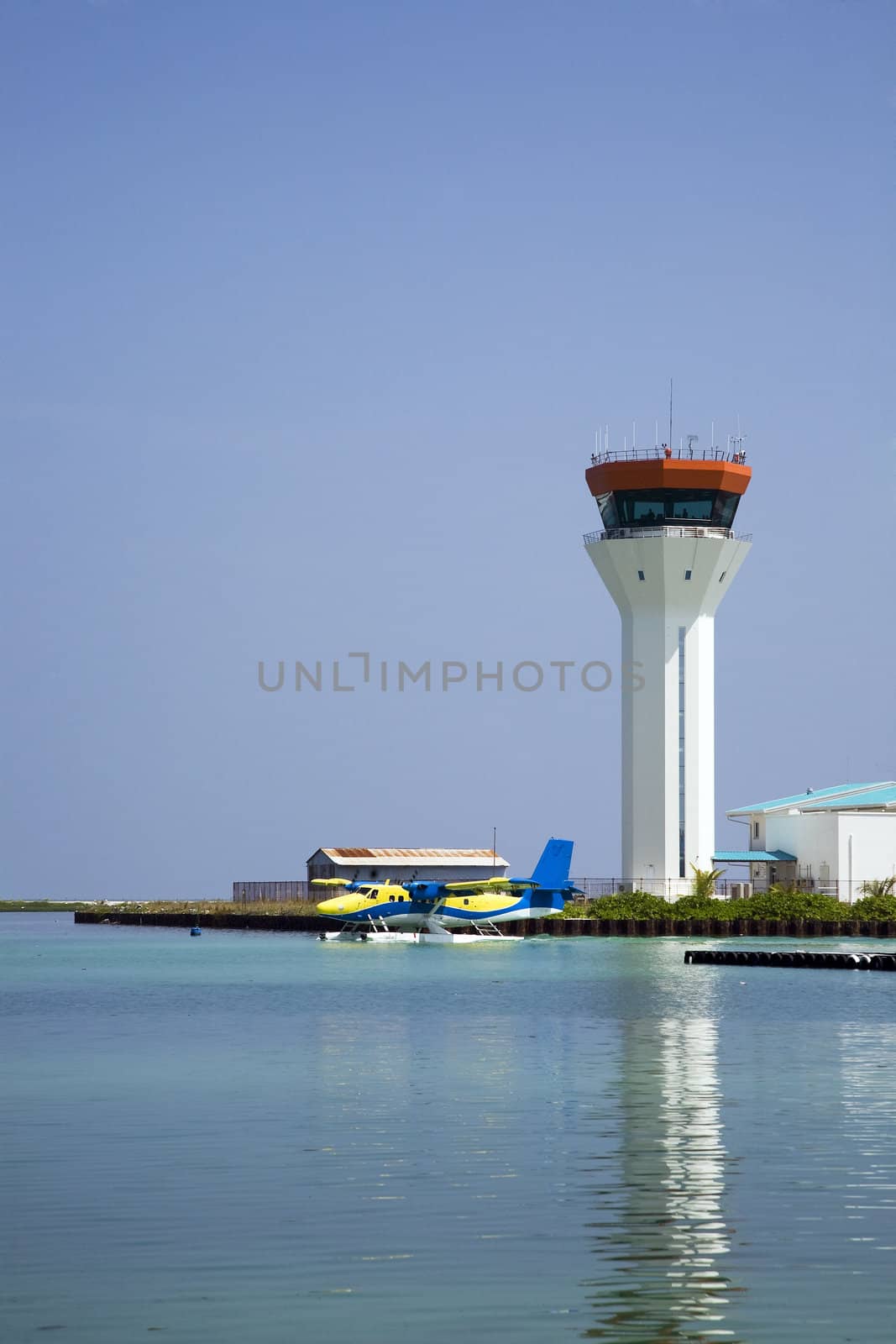 A sea plane lands on the water with the air traffic control tower in the background.