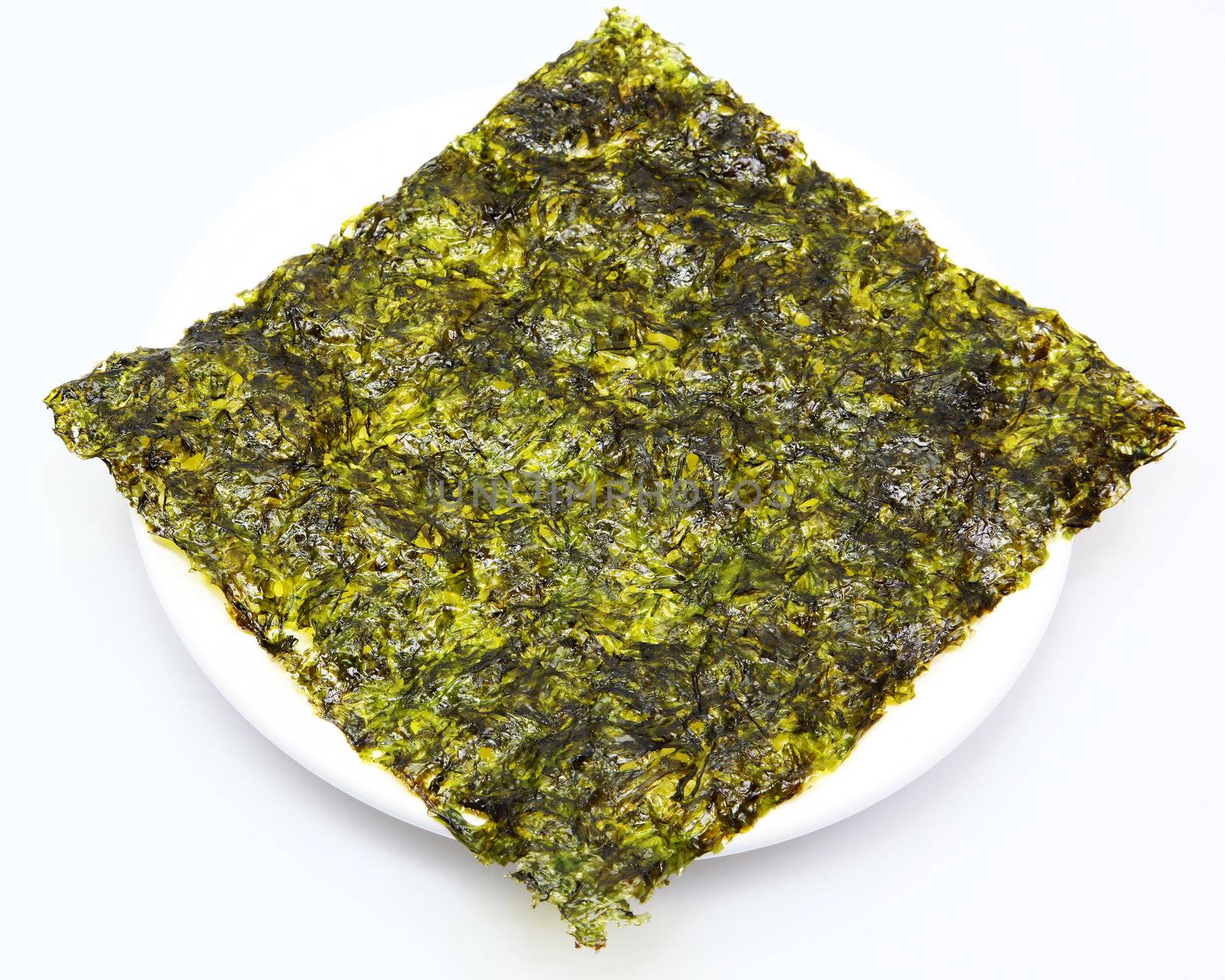 Large thin sheet of pressed seaweed pan fried in olive oil in a white plate.