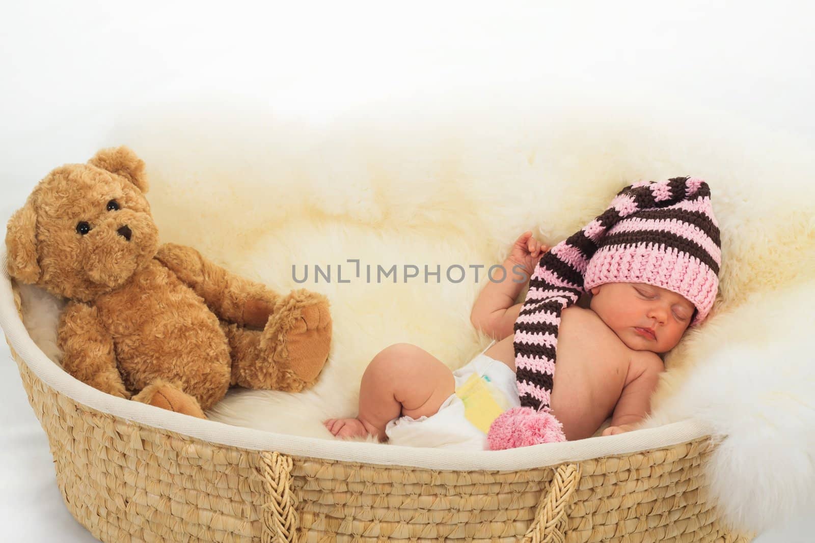 infant sleeping on a white sheepskin in a wicker basket.