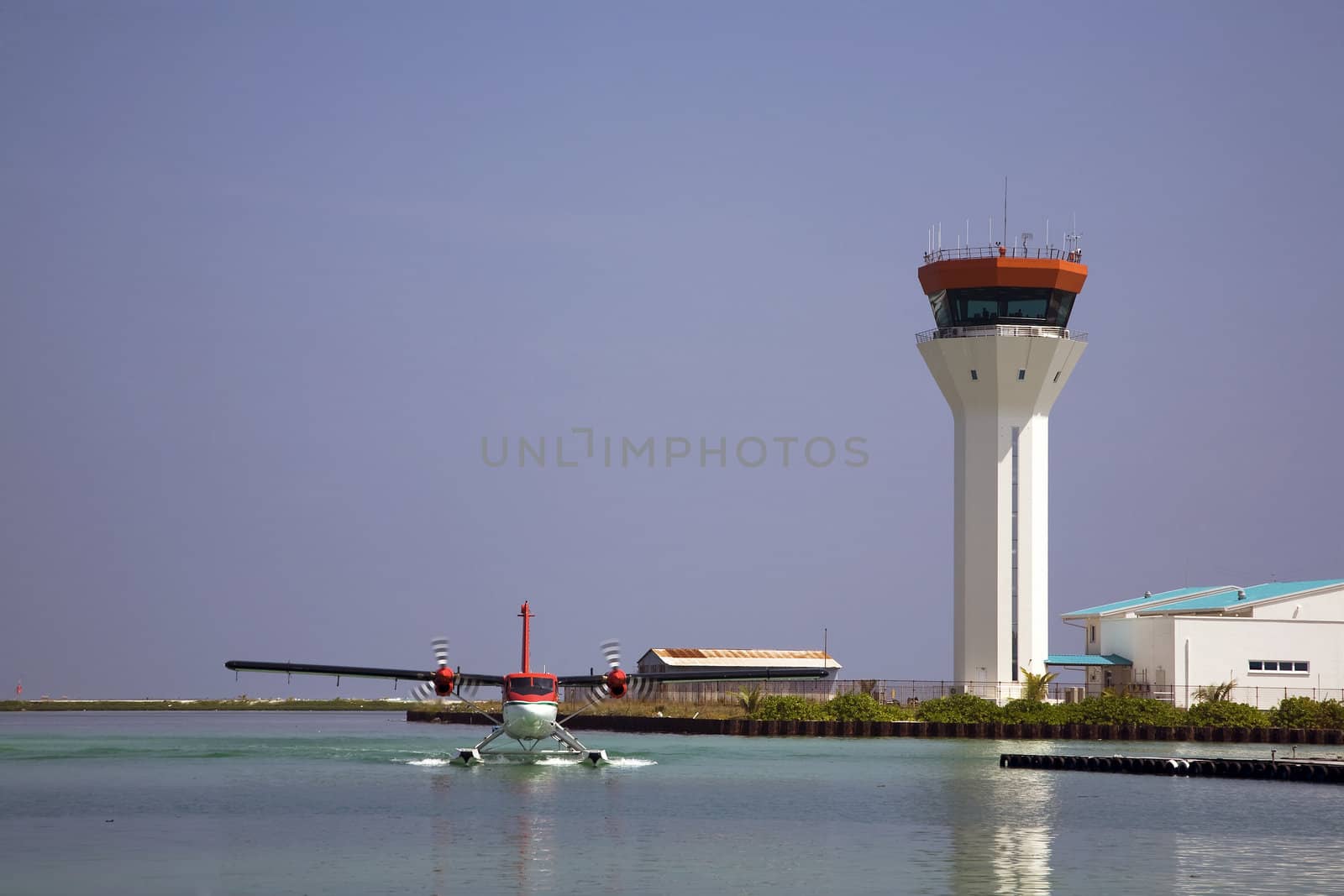 A sea plane lands on the water with the air traffic control tower in the background.