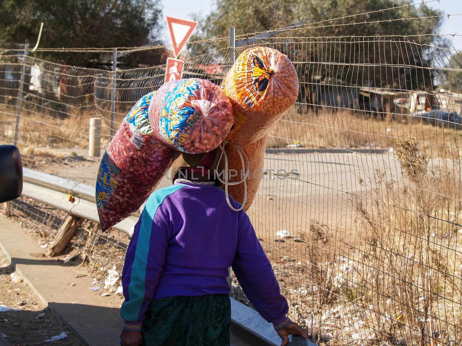 Lady walking away with two large bags of material, walking through the poor area of Soweto.