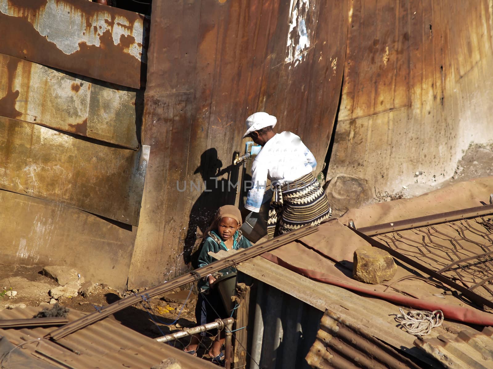 Woman obtains water from standpipe outside a Soweto shanty town shack, while child looks on.







Woman get water from standpipe amongst the rusty iron homes in the Soweto squatter village.