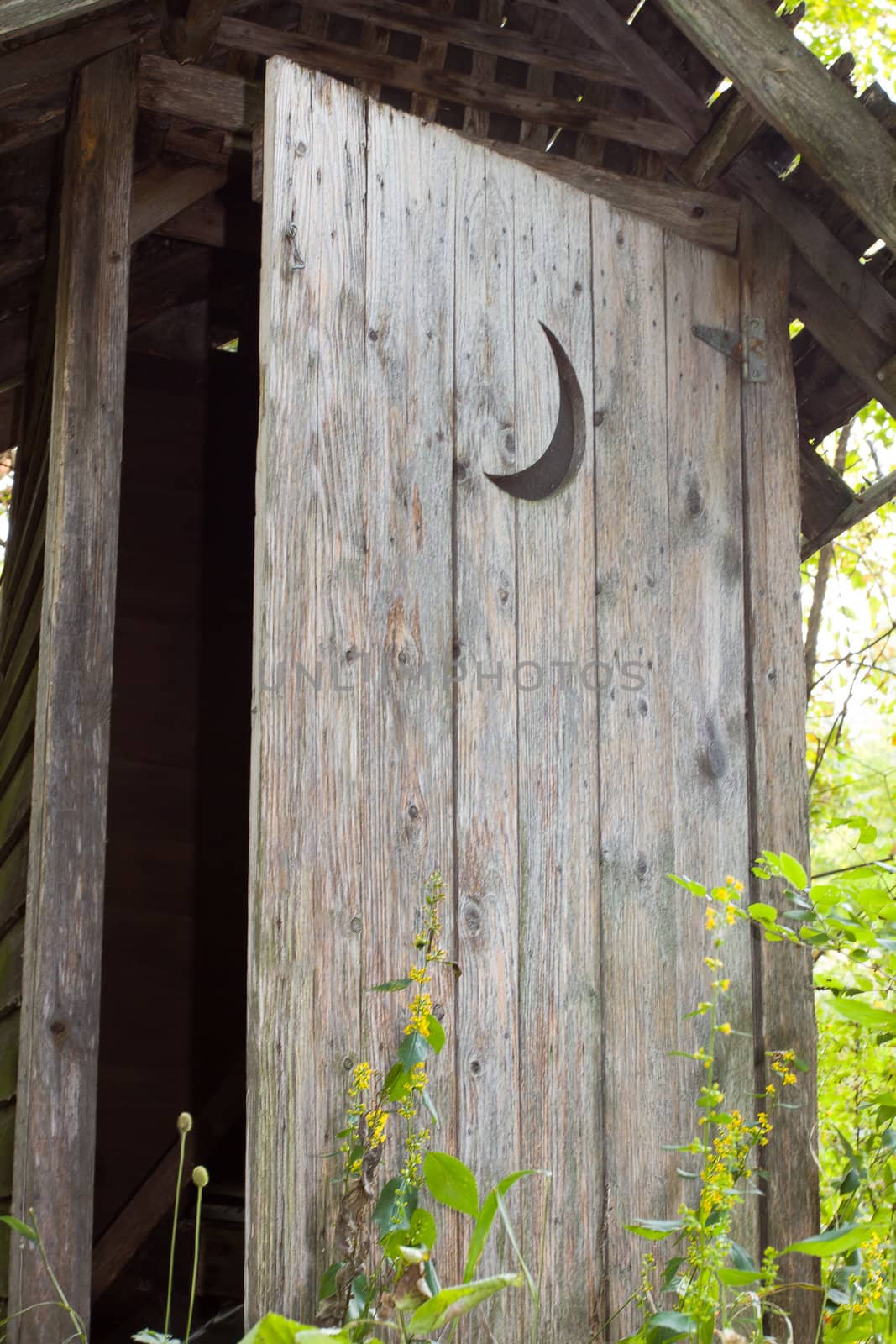 A crescent moon adorns an abandoned outhouse