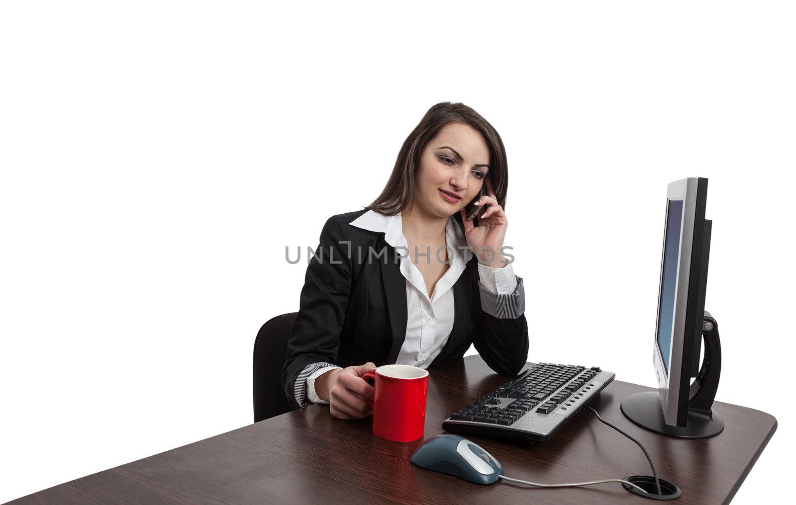 Portrait of a young brunette businesswoman with a red cup using a mobile phone at her desktop in an office.