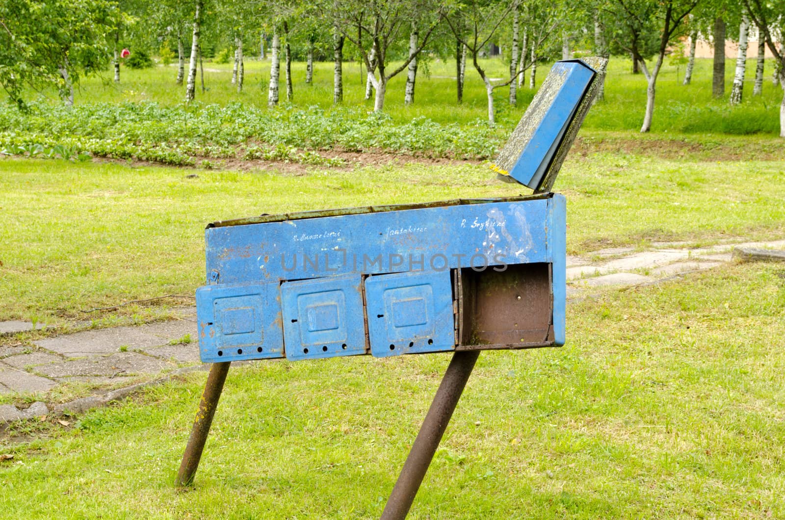 Retro blue rusty postbox with names on it and rural agricultural field and trees.