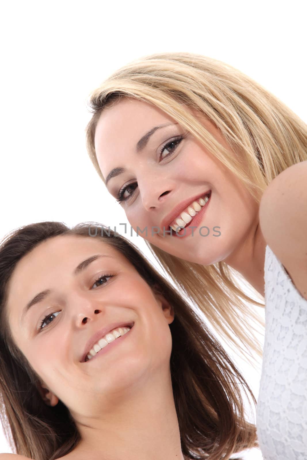 Low angle view of the faces of two attractive smiling women standing with their heads close together isolated on white Low angle view of the faces of two attractive smiling women standing with their heads close together isolated on white