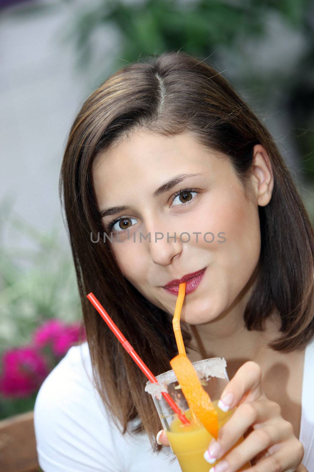 Beautiful woman drinking a glass of freshly squeezed healthy orange juice or cocktail through a straw with obvious enjoyment 