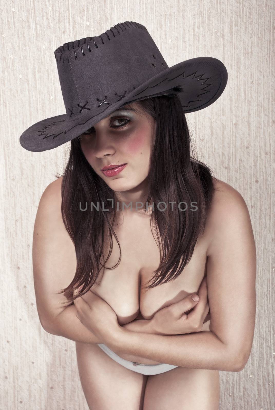 Beautiful sexy brunette in a cowboy hat, with his body covering his chest with his hands.