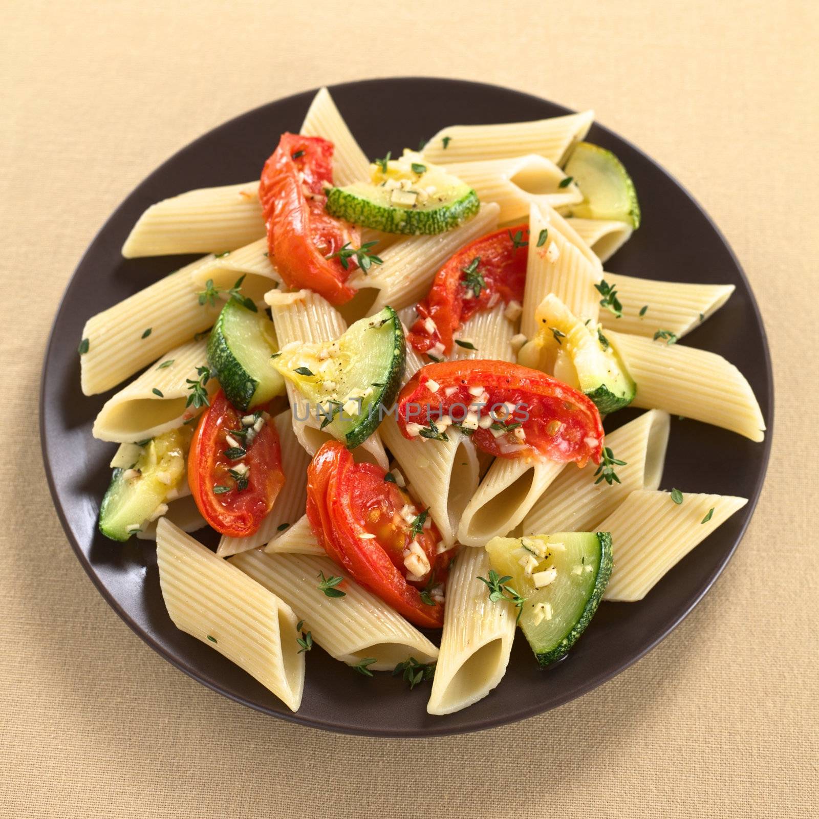 Vegetarian penne pasta dish with baked zucchini and tomato spiced with thyme and garlic (Selective Focus, Focus on the lower part of the dish)