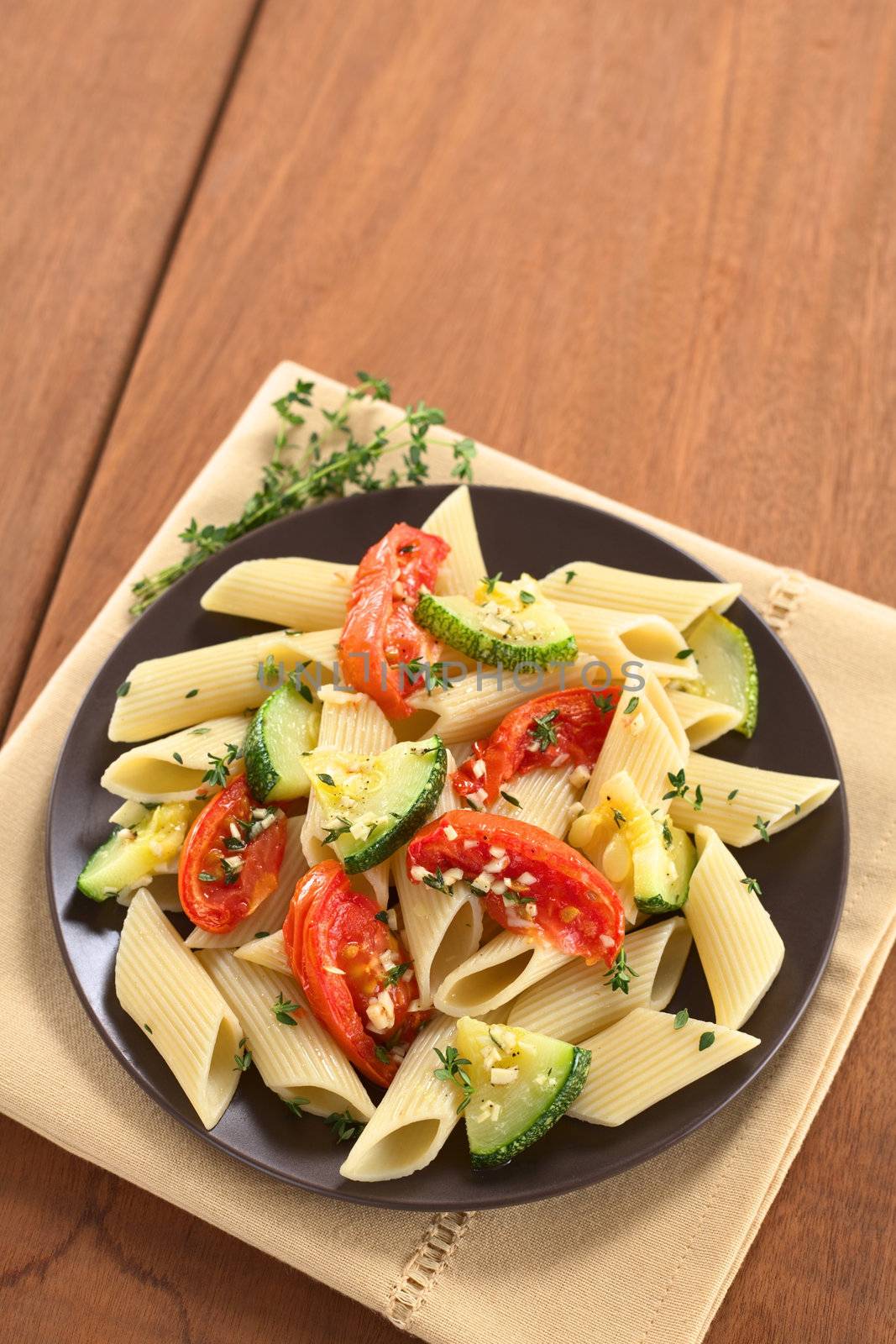 Vegetarian penne pasta dish with baked zucchini and tomato spiced with thyme and garlic (Selective Focus, Focus on the lower part of the dish)