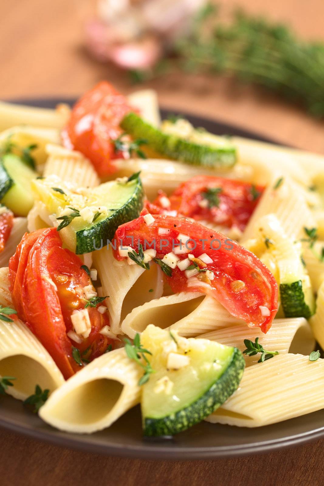 Vegetarian penne pasta dish with baked zucchini and tomato spiced with thyme and garlic (Selective Focus, Focus one third into the pasta dish)