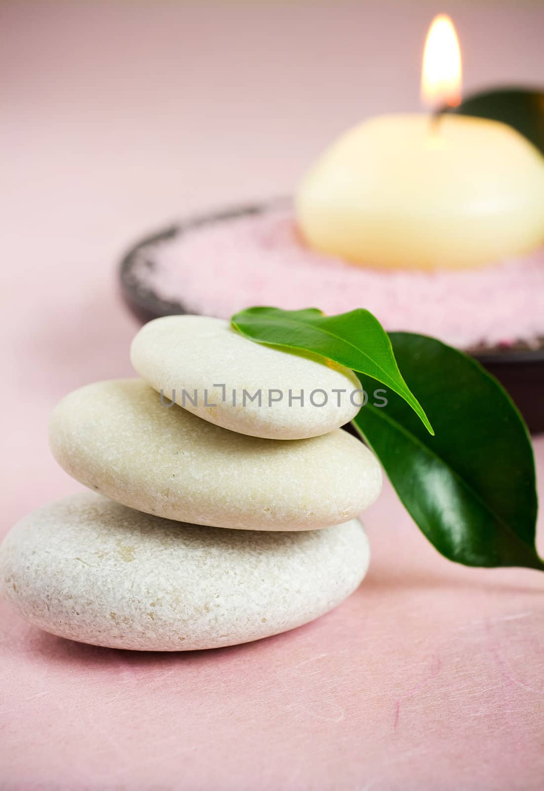 White zen stones, green leaves,  candle,  sea salt, pink background.