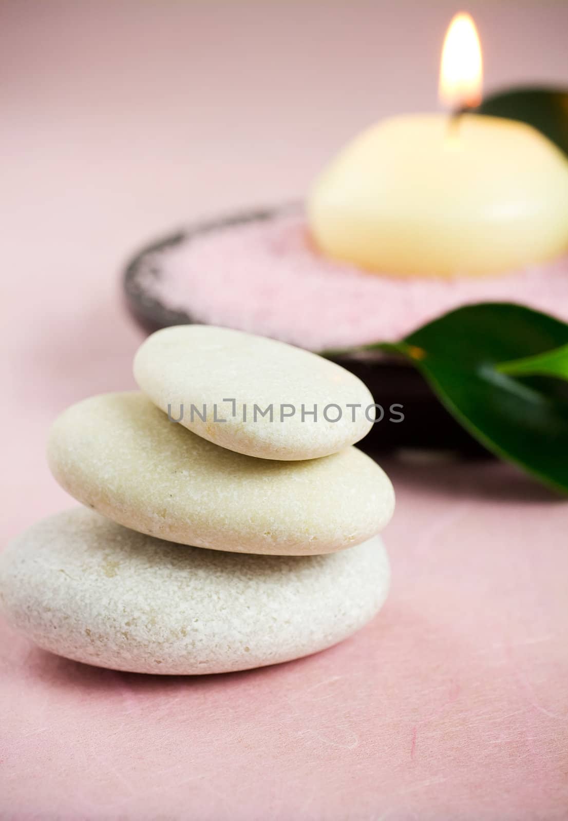 White zen stones, green leaves,  candle,  sea salt, pink background.