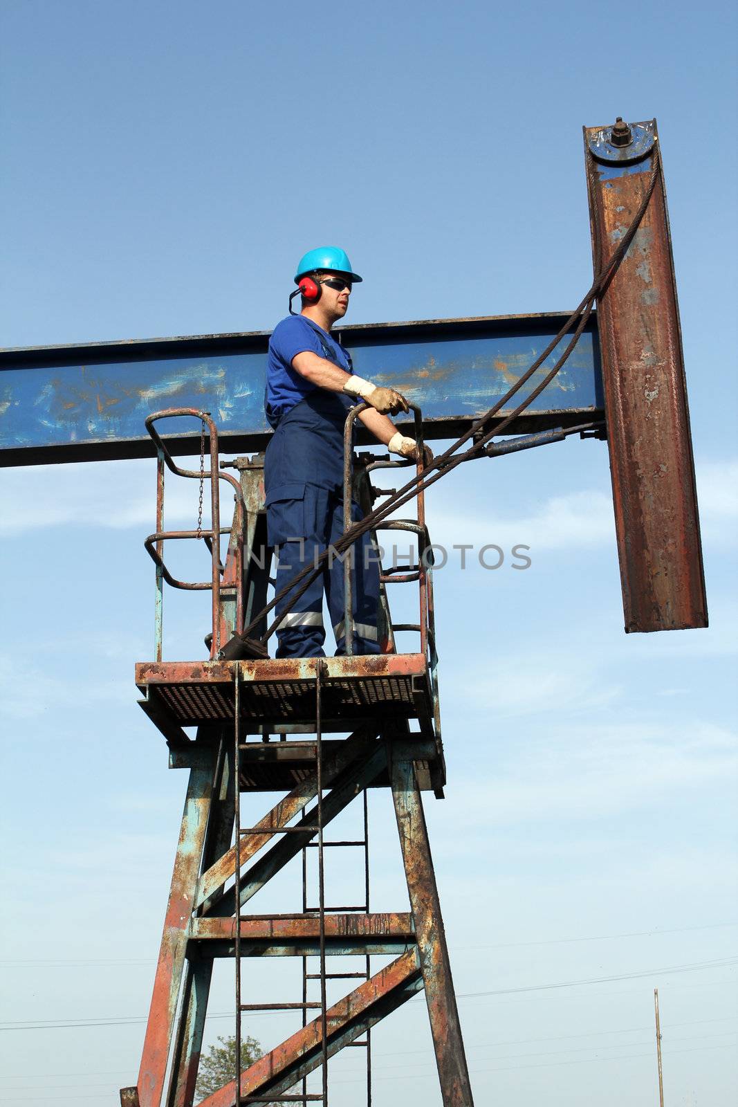 oil worker in blue uniform standing at pump jack by goce