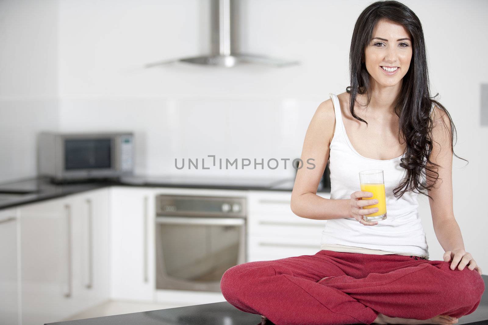 Young woman sitting on counter drinking orange juice
