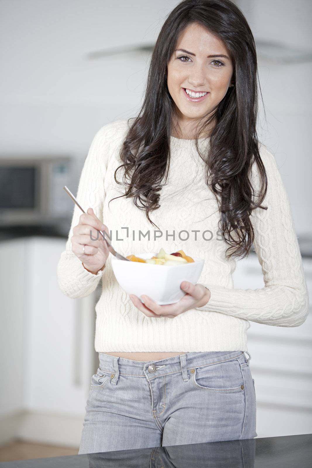 Young woman enyoying a bowl of fresh fruit in her kitchen