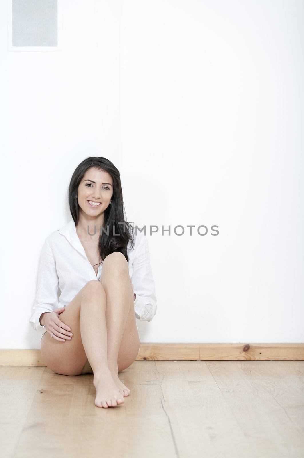 Young woman in underwear sitting against white wall at home