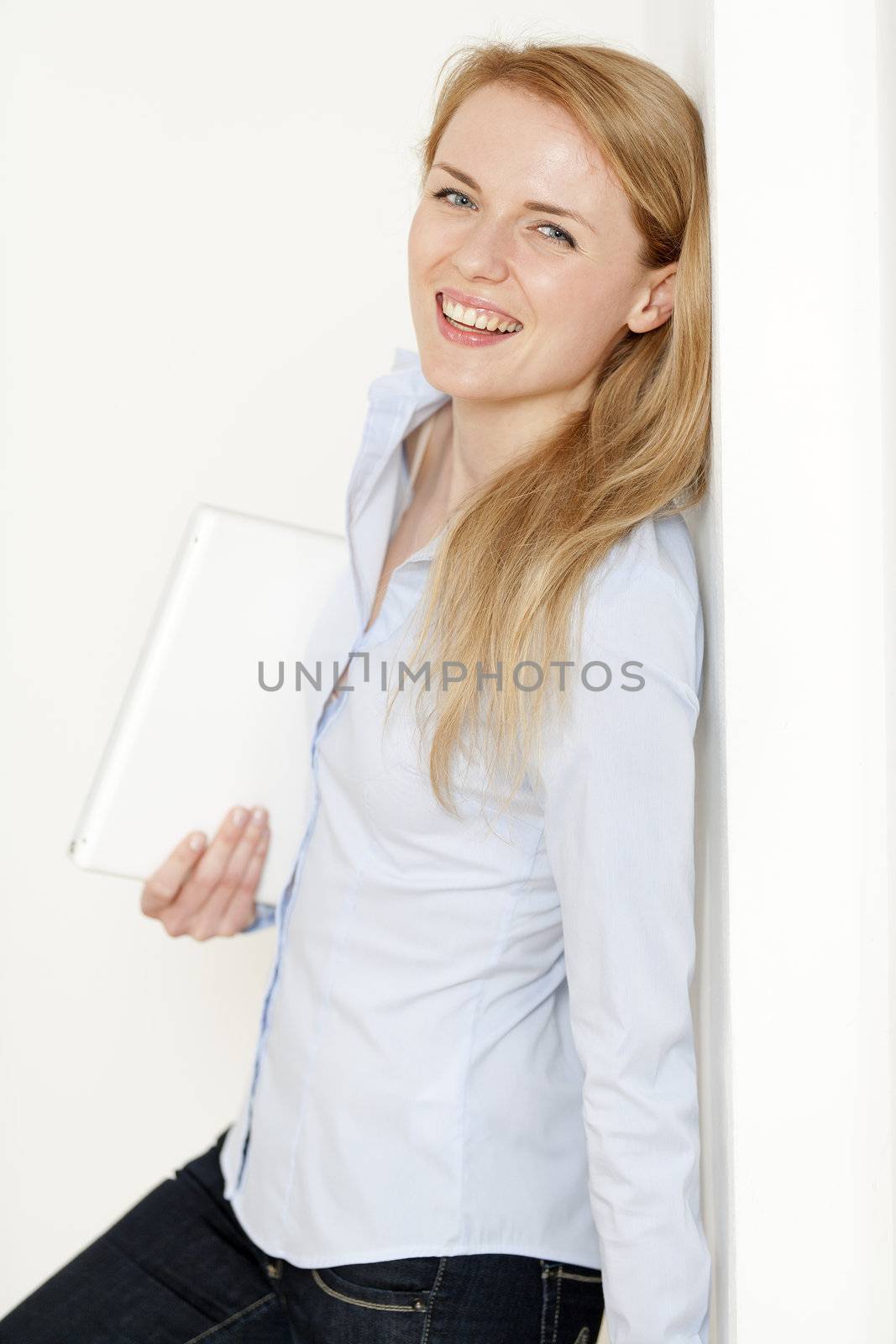 Young woman leaning against a white wall holding a white laptop computer