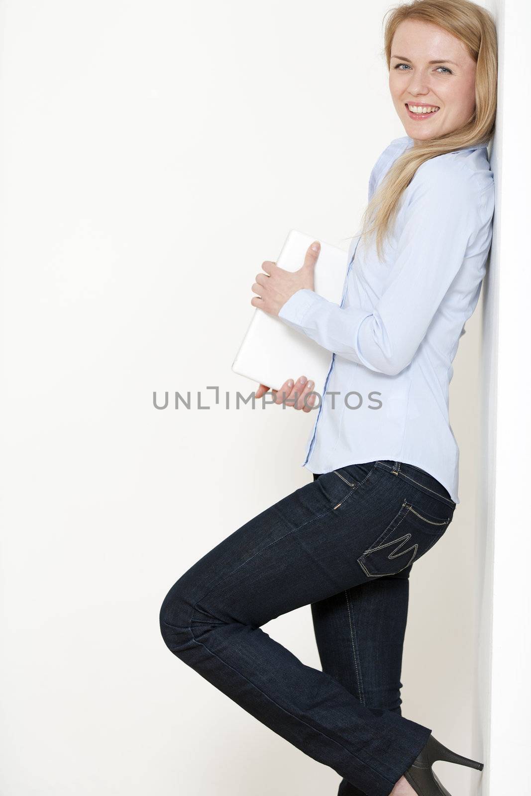 Young woman leaning against a white wall holding a white laptop computer