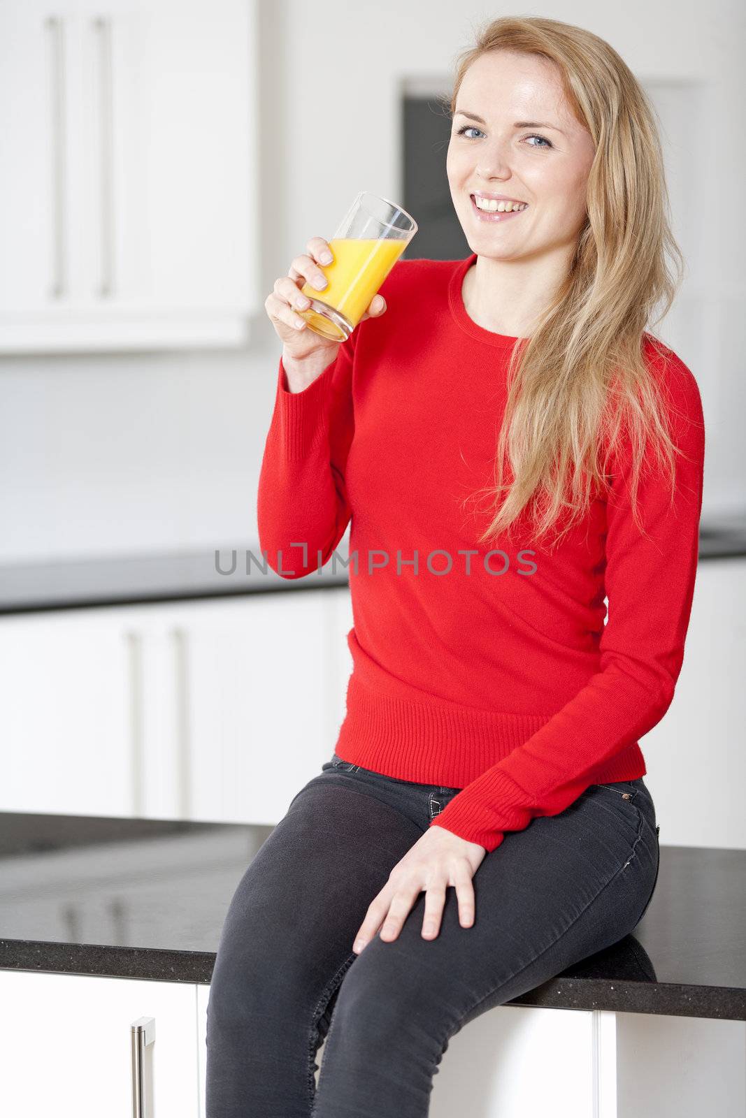 Young woman sitting on counter drinking orange juice