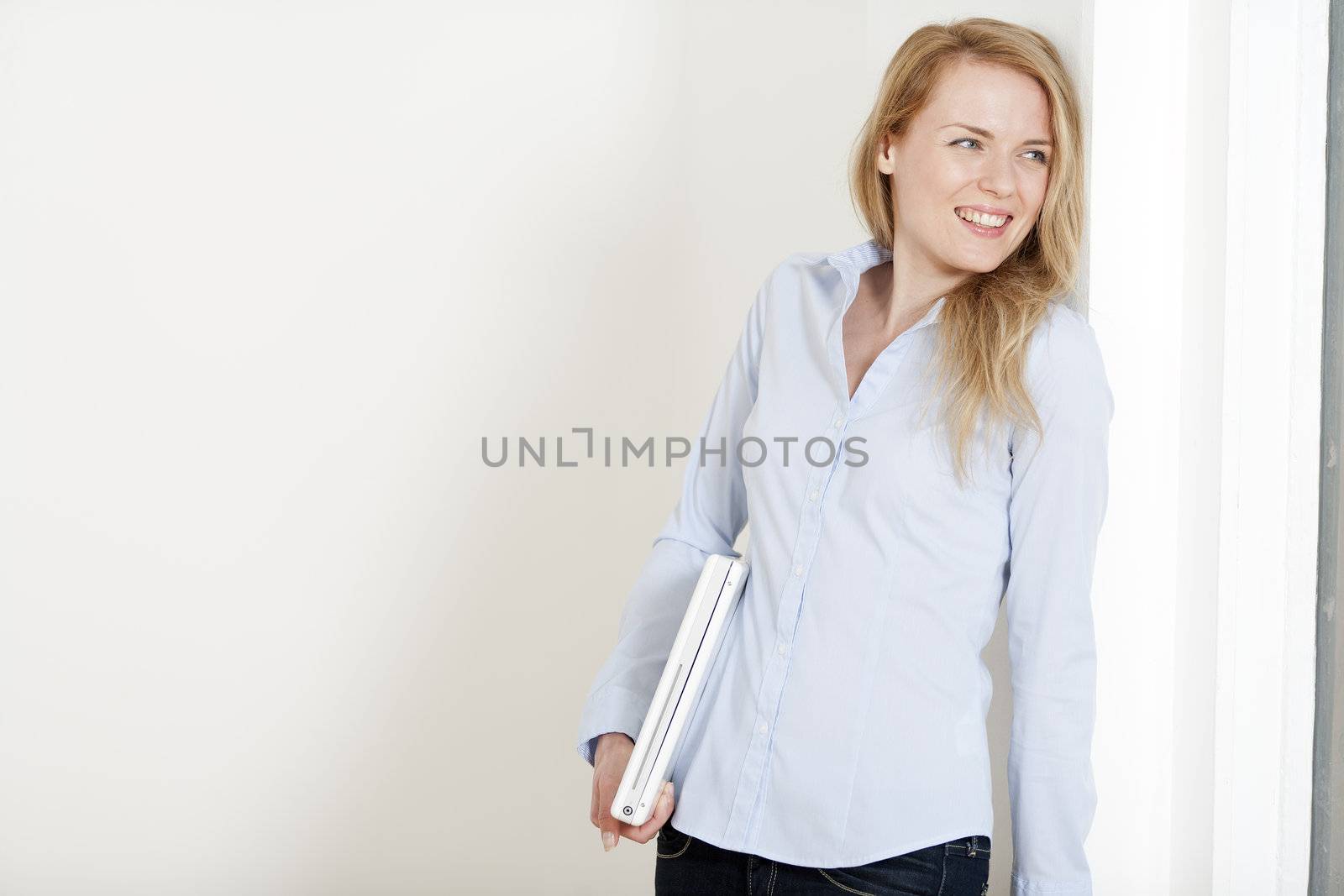 Young woman leaning against a white wall holding a white laptop computer
