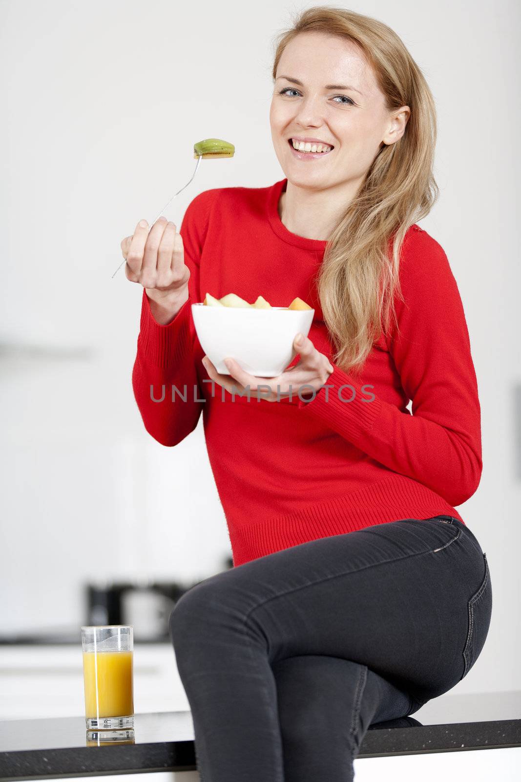 Young woman enjoying a bowl of fresh fruit in her kitchen with orange juice