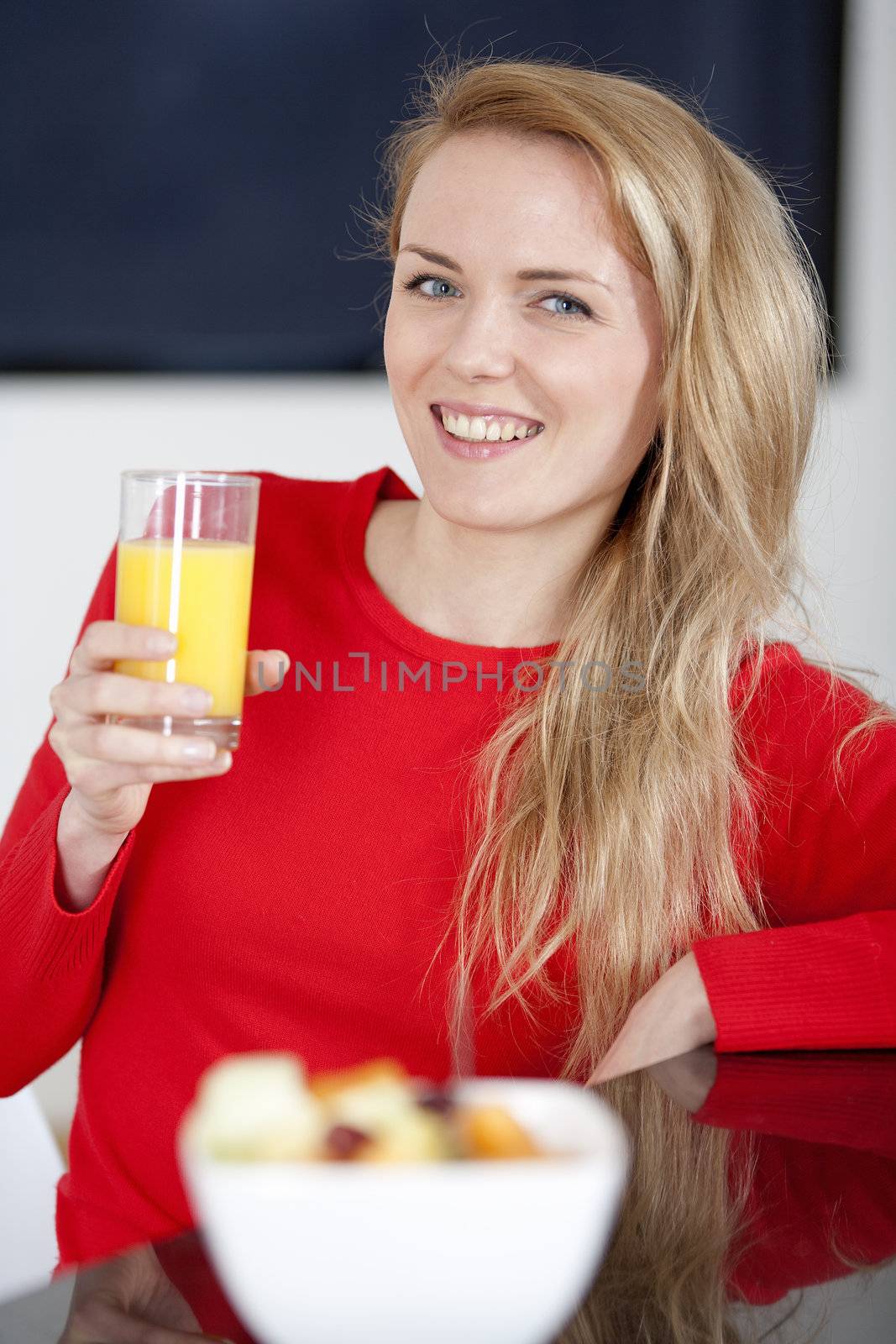 Young woman enjoying a bowl of fresh fruit in her kitchen with orange juice