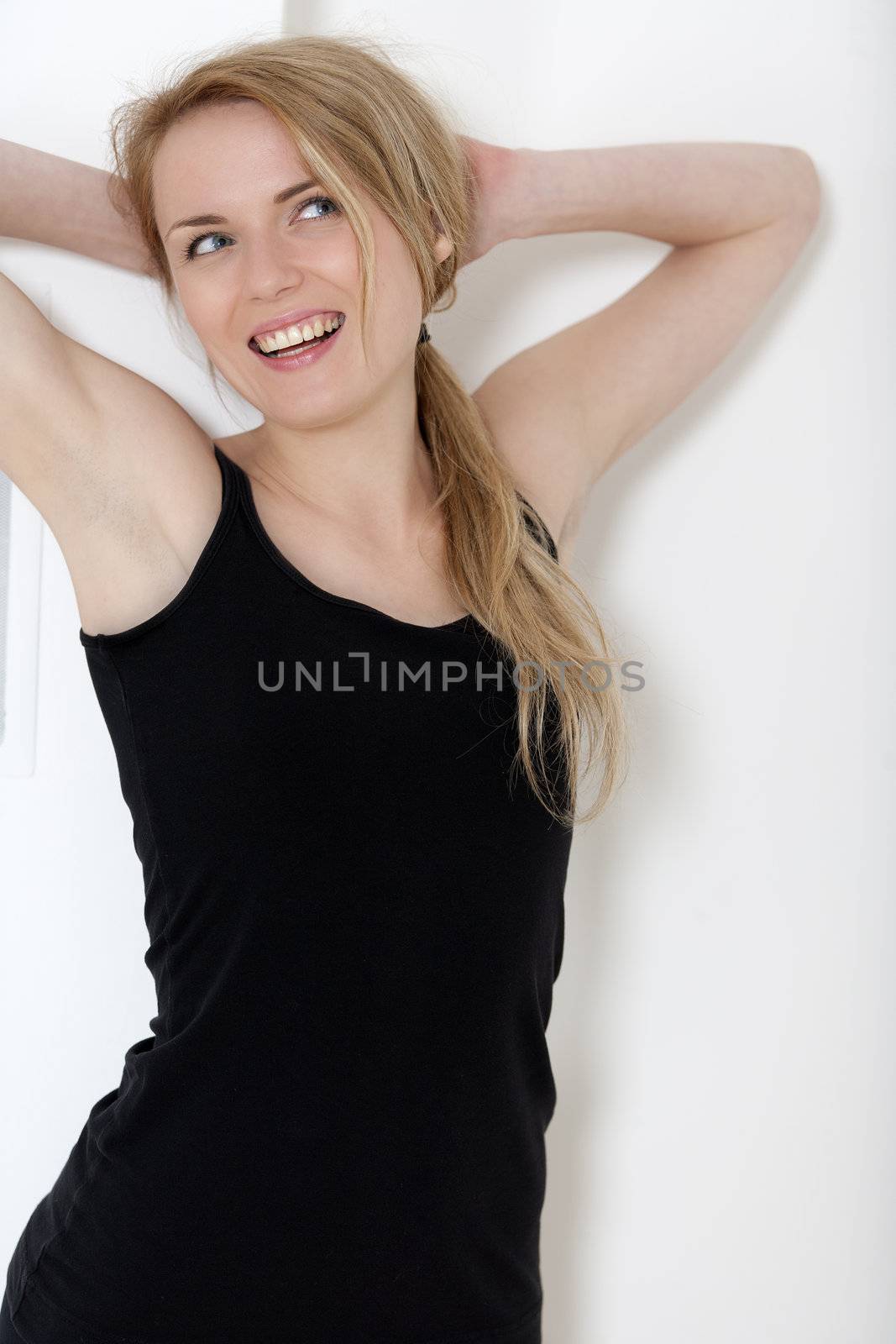 Young woman at home leaning against a white wall in black fitness wear.