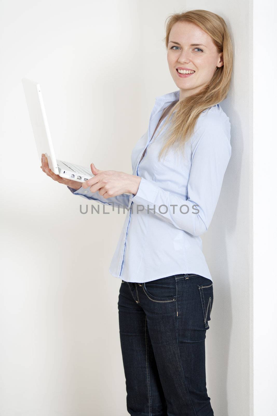 Young woman leaning against a white wall holding a white laptop computer