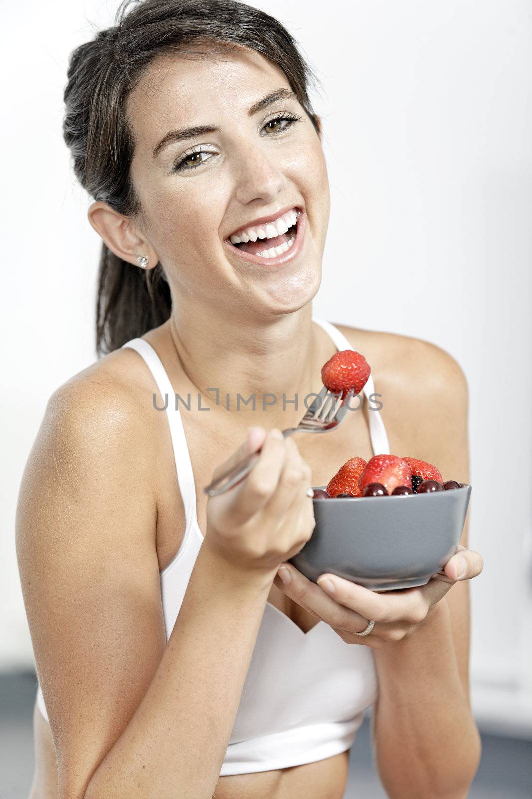 beautiful young woman in fitness clothes eating fresh fruit from a bowl at home