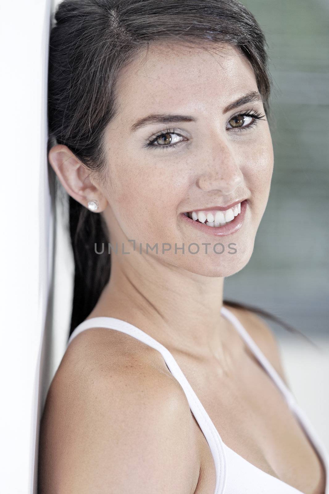 Beautiful young woman leaning against white wall resting after exercise