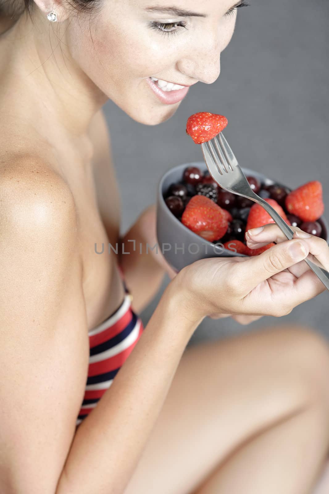 Beautiful young woman enjoying fresh fruit for breakfast in a red bikini