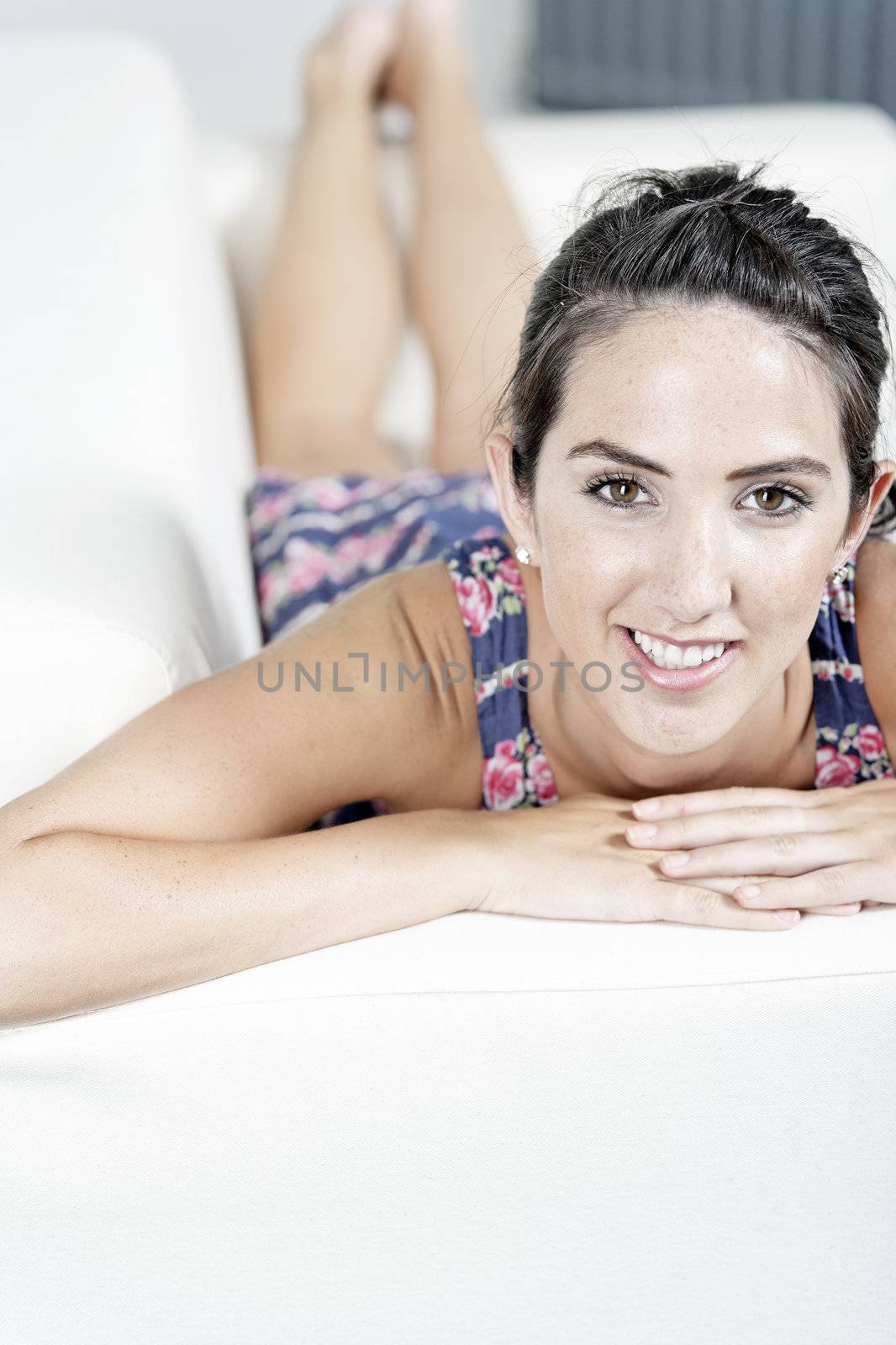 Beautiful young woman wearing a blue summer dress resting on her sofa at home