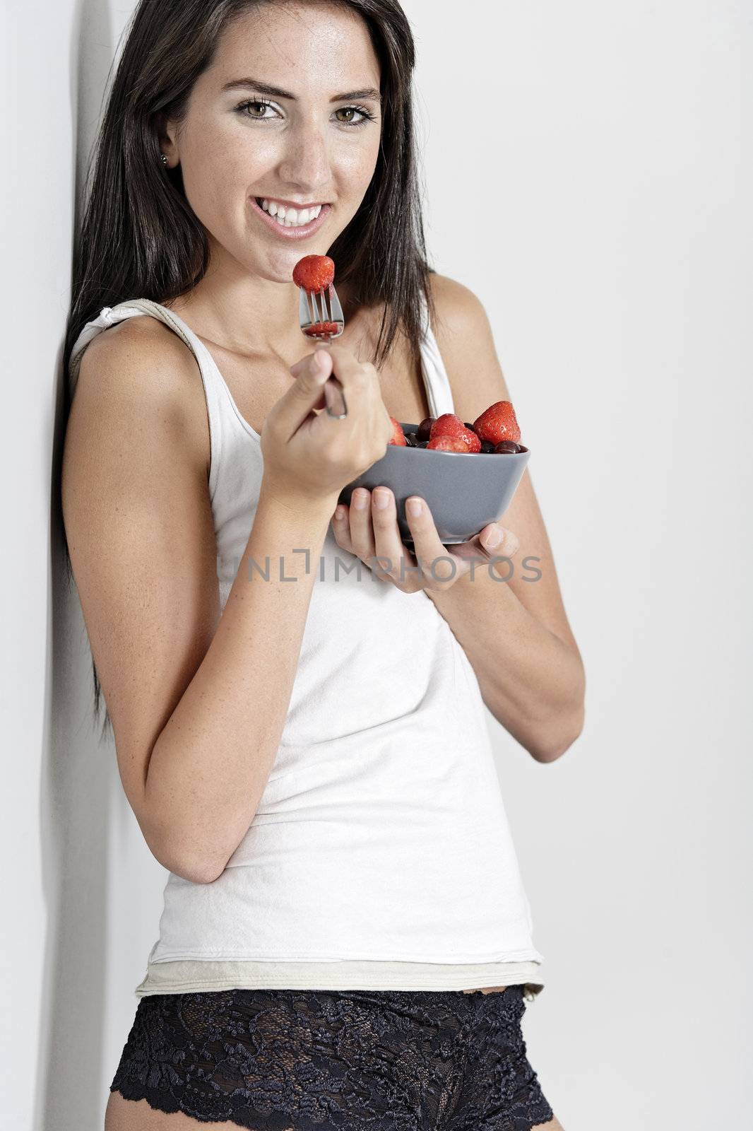 Beautiful young woman in underwear leaning against a wall enjoying a fruit salad