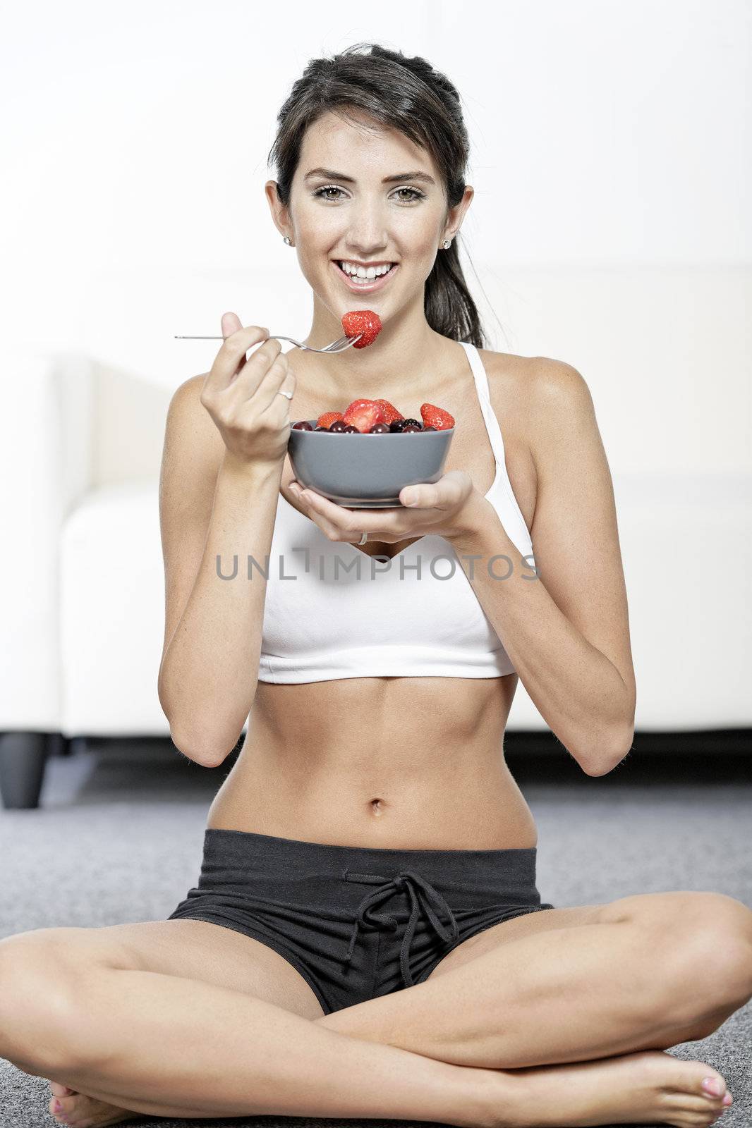 beautiful young woman in fitness clothes eating fresh fruit from a bowl at home