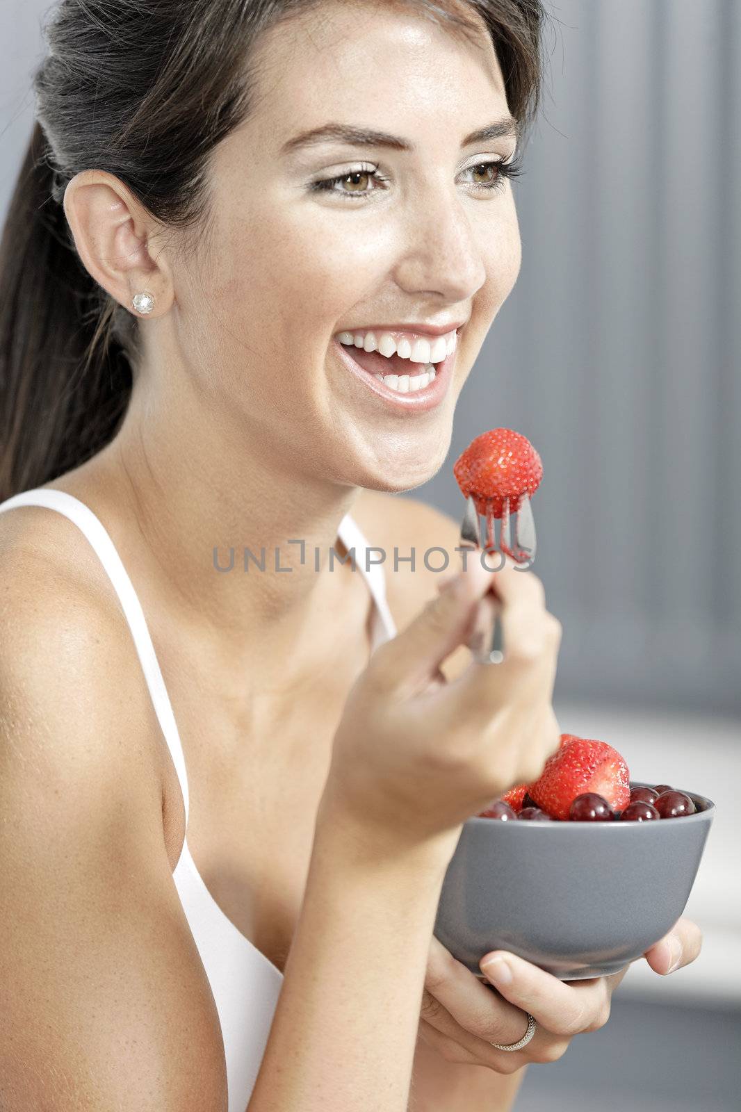 beautiful young woman in fitness clothes eating fresh fruit from a bowl at home