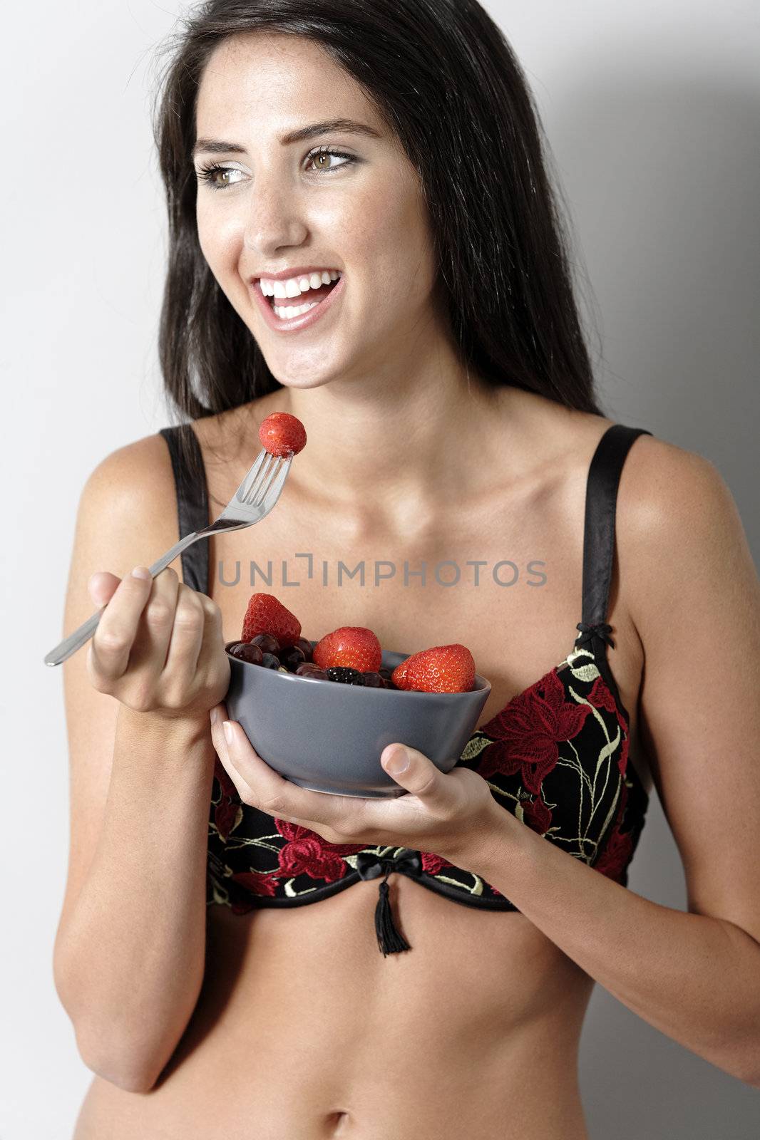 Beautiful young woman in underwear leaning against a wall enjoying a fruit salad
